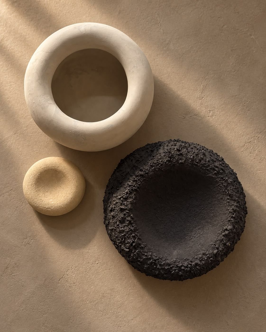 Ivory ring-shaped ceramic vessels and a black textured bowl in warm sunlight